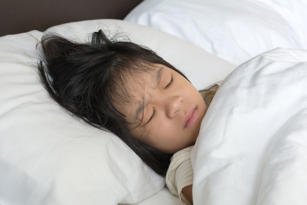 A young girl tucked into bed with a frown on her face