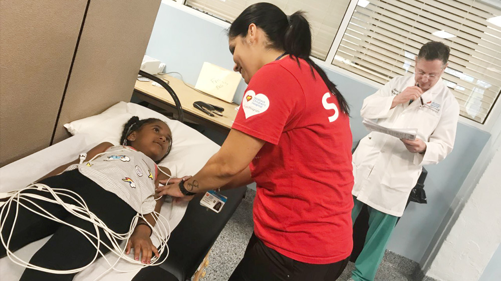 técnica colocando sensores en una niña acostada en la mesa de exploración.