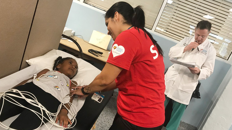 técnica colocando sensores en una niña acostada en la mesa de exploración.