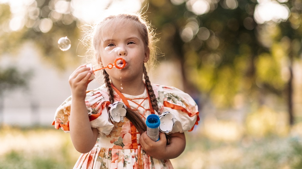 Young girl with genetic disorder blowing bubbles outside in grass