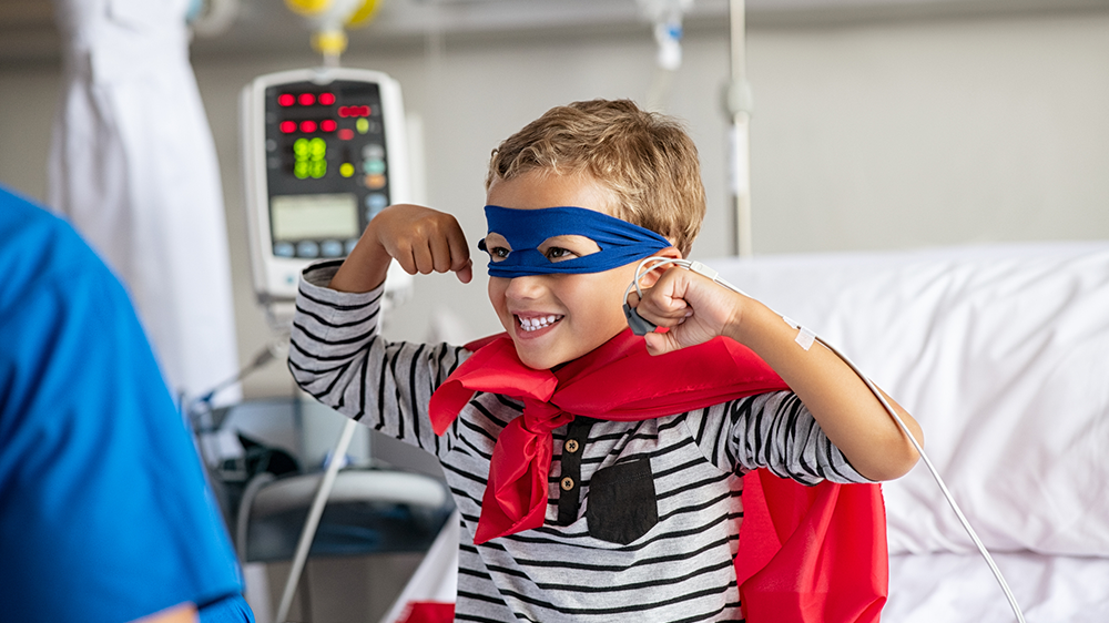 Niño fuerte en cama de hospital vestido de superhéroe