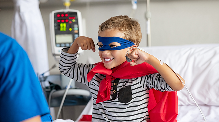 Strong young boy in hospital bed dressed as superhero