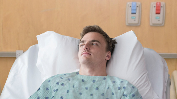 young man looking pensive while laying on hospital bed.