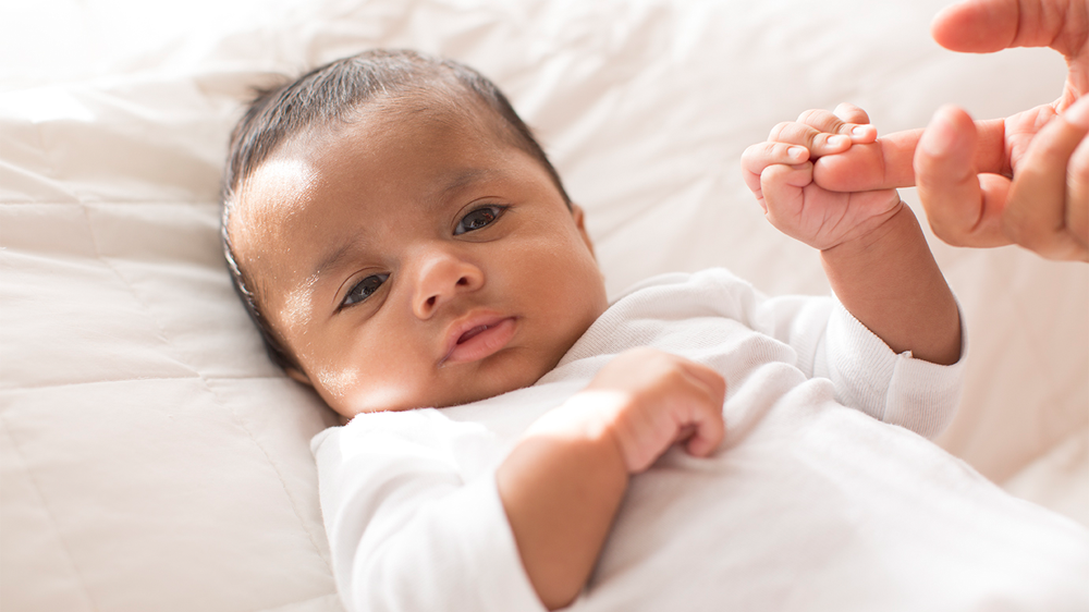 infant clasping the index finger of parent.