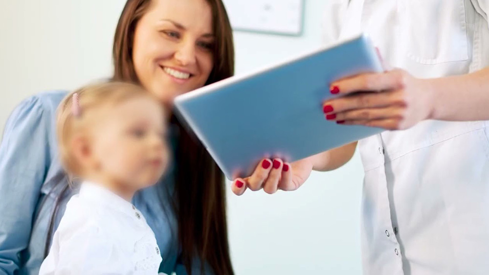 nurse is showing a mother with young baby daughter a tablet screen