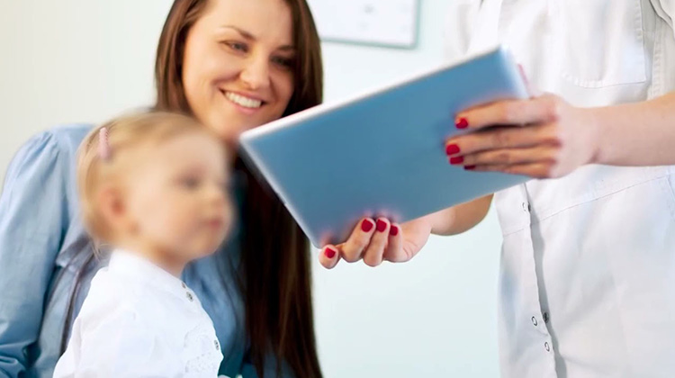 enfermera le muestra a una madre con una hija pequeña la pantalla de una tableta