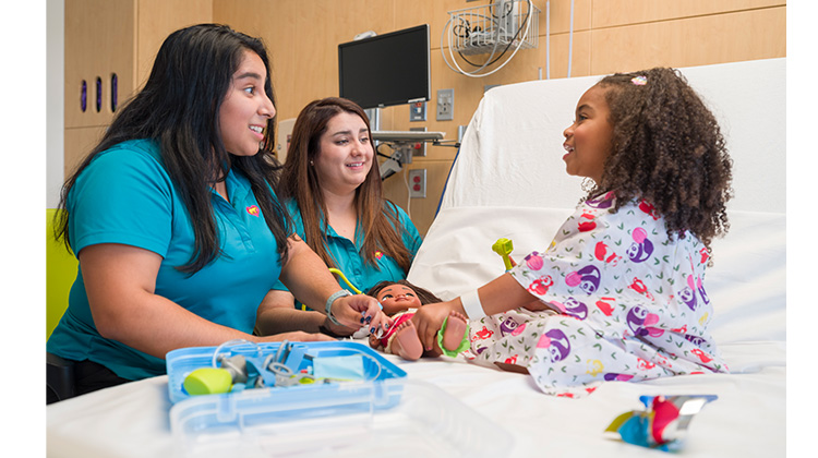 2 especialistas de vida infantil juegan con niña hospitalizada.