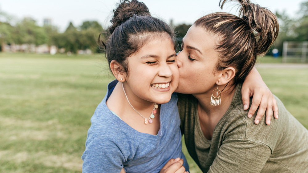 smiling girl being kissed on the cheek by her mother