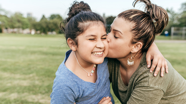 niña sonriente mientras su madre besa su mejilla