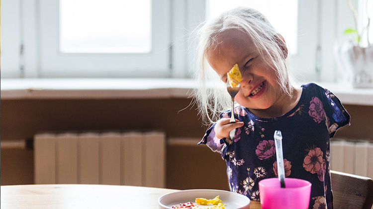 una niña sin brazos y con dos dedos en la mano sostiene con orgullo un tenedor mientras desayuna.
