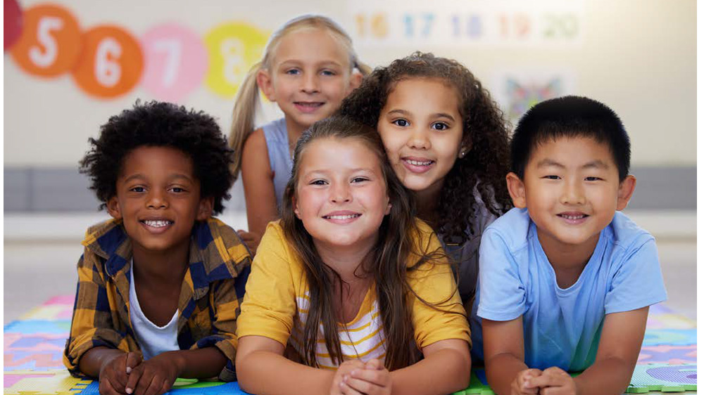 group of children of different ethnicities smile in a classroom.