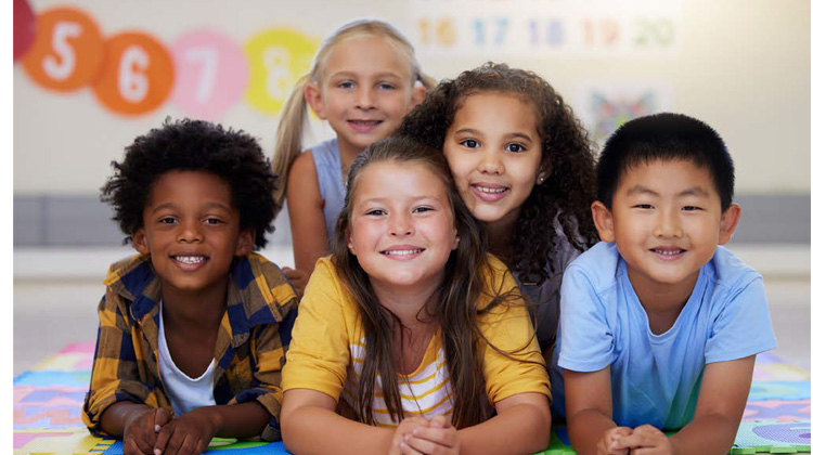 group of children of different ethnicities smile in a classroom.