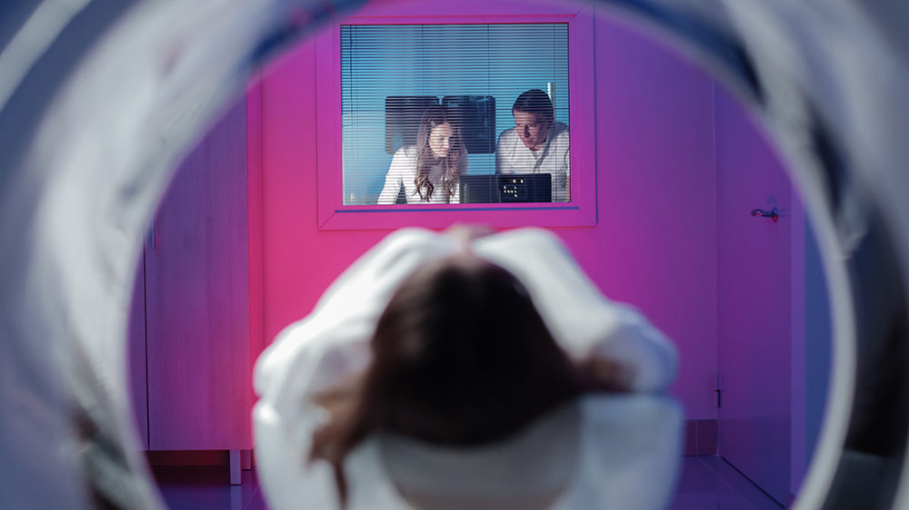 view of girl entering MRI scan machine, doctors on the other side monitor the procedure.