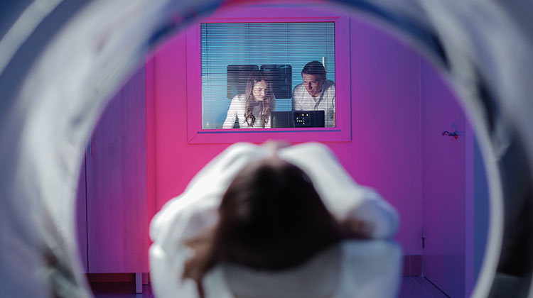 view of girl entering MRI scan machine, doctors on the other side monitor the procedure.