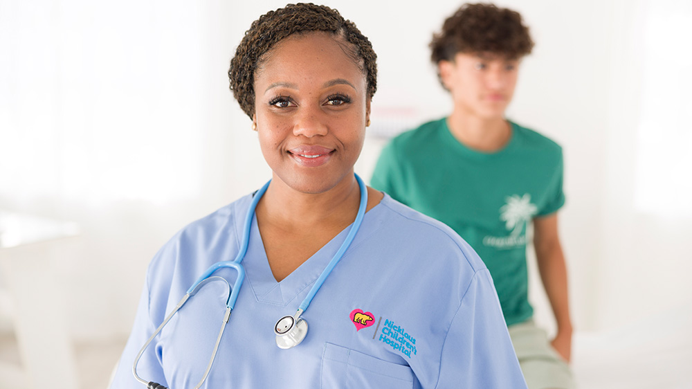 smiling nurse wearing light blue scrubs.