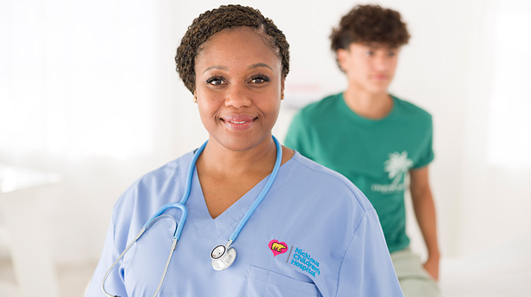 smiling nurse wearing light blue scrubs.