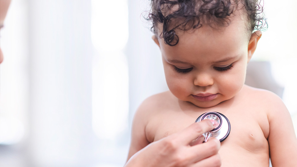 baby looks down as a hand places stethoscope to their chest