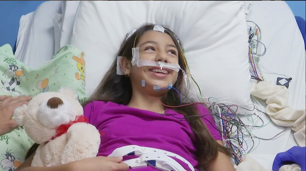 Girl with long hair in bed with electrodes on her forehead ready for her sleep study.