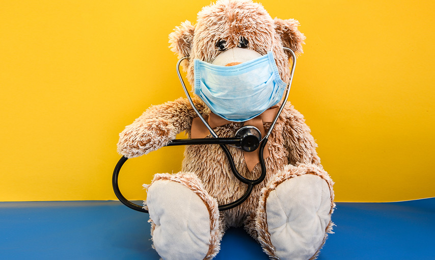 teddy bear with wearing a facemask holding stethoscope to his own heart.