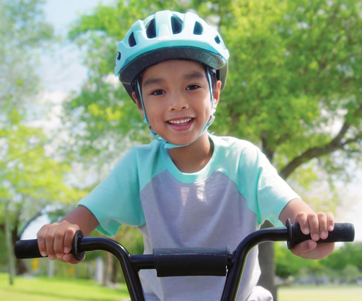 boy riding his bicycle on a sunny day wearing safety helmet.