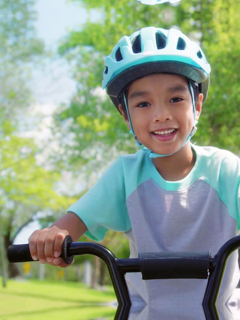 boy riding his bicycle on a sunny day wearing safety helmet.