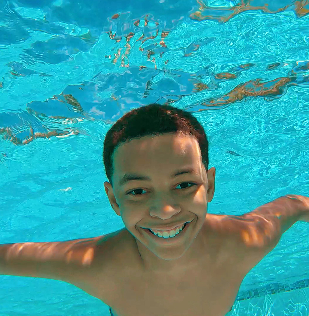 boy submerged in swimming pool smiling for the camera.