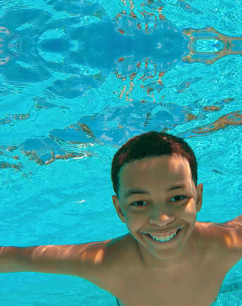 boy submerged in swimming pool smiling for the camera.