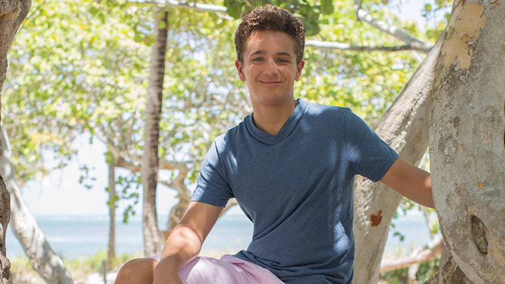 Andrew posing for a photo in front of a body of water near a tree. 