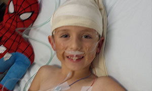 Jimmy in his hospital bed smiling next to a stuffed spider man doll. 