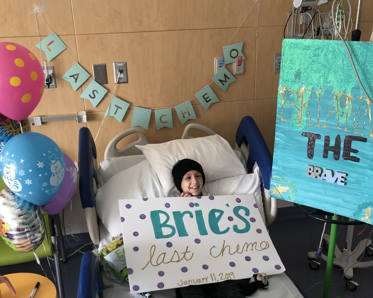 Brianna in a hospital bed with signs that say, Bries, last chemo January 11, 2019