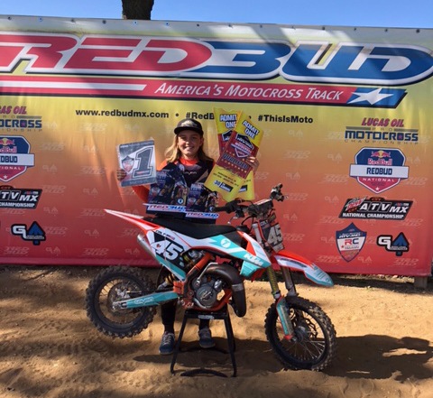 Colt posing in front of a dirt bike while holding up awards