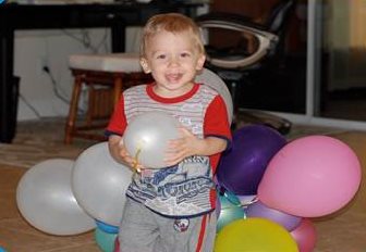 Toddler Asher, playing with balloons while smiling for the camera. 
