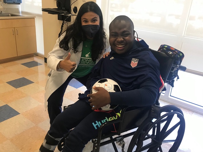 Jabarry in a wheelchair holding a soccer ball smiling next to Dr. Payares. 