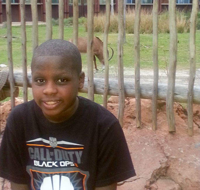 Myles at the zoo smiling in front of an animal exhibit. 