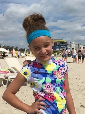 Stephanie at the beach, smiling while she poses for a photo with her hand on her hip.