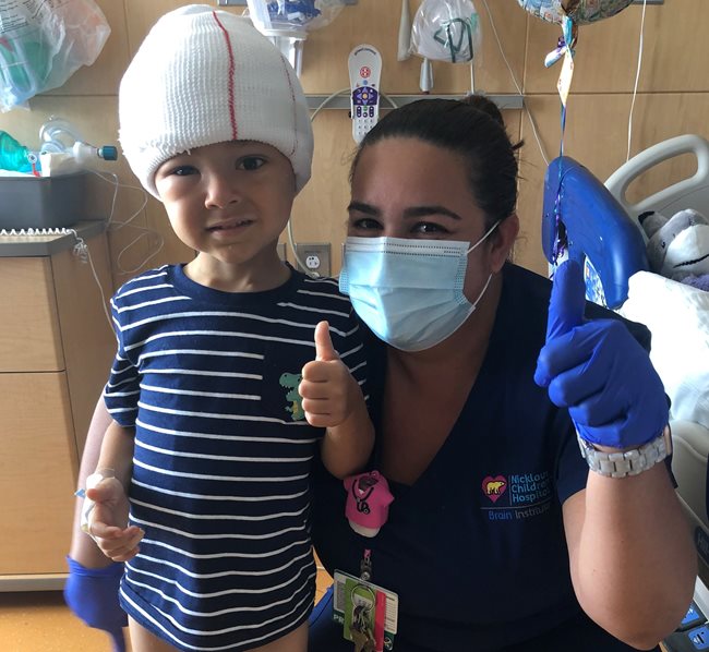 Jayden giving a thumbs up next to a clinician while standing in his hospital room. 