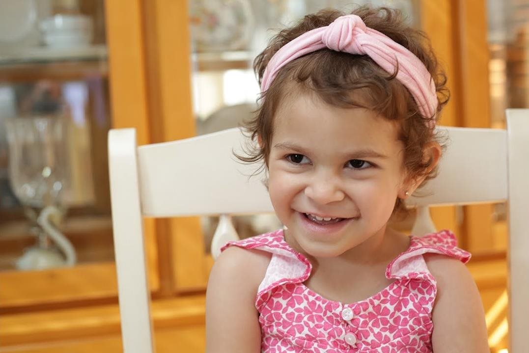 Lacy smiling while sitting in a wood dining chair.