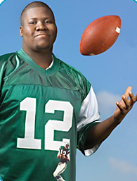 St. Clair wearing a football jersey throwing a football up in the air with one hand. 