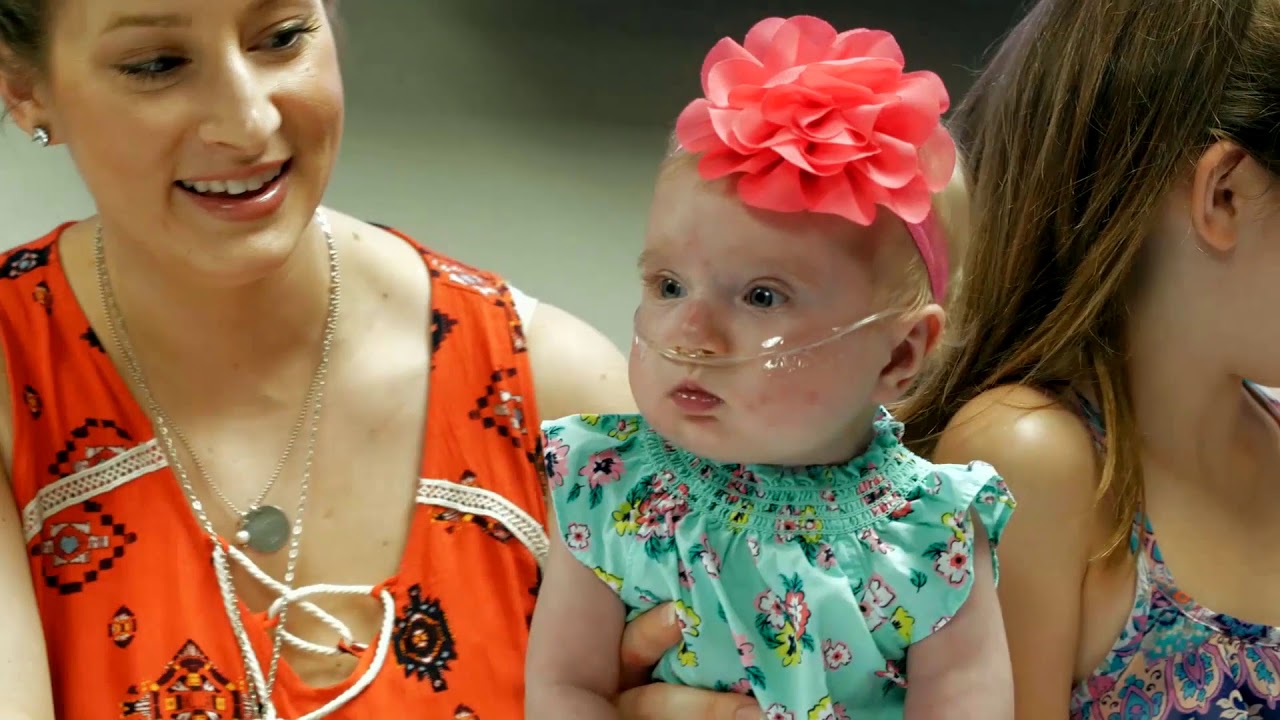 Teegan wearing a floral dress and her mother holds her.