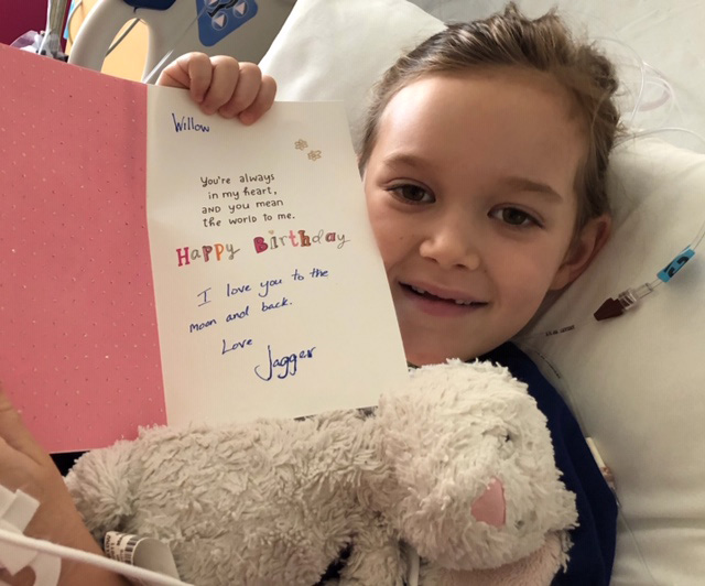 Willow holding up her birthday card while in her hospital bed.