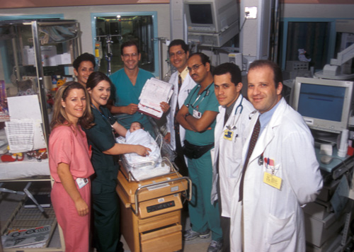 group of doctors and nurses gathered around a newborn baby in an incubator.