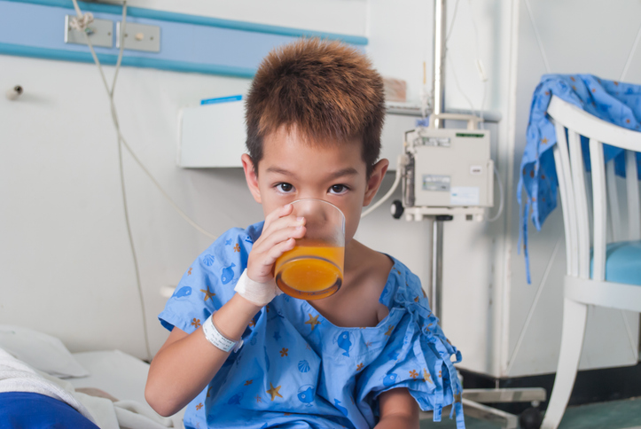 boy drinking juice while still wearing hospital gown.