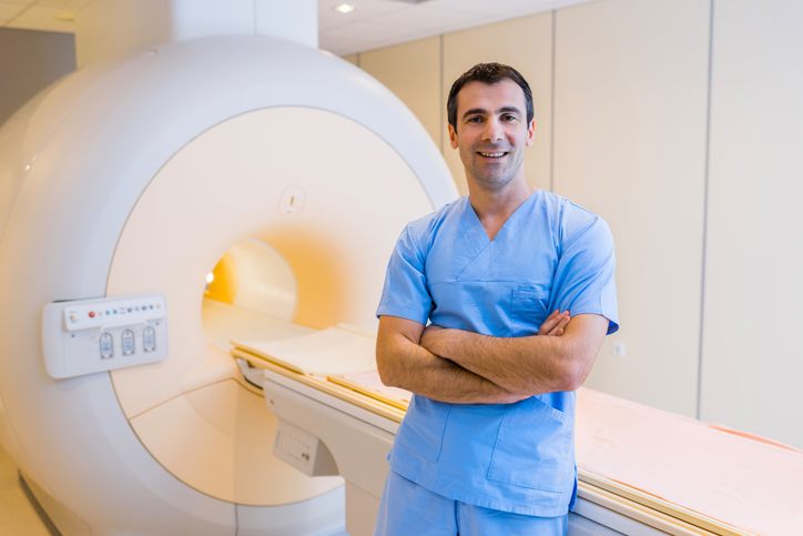 male technician stands by MRI machine with arms crossed.
