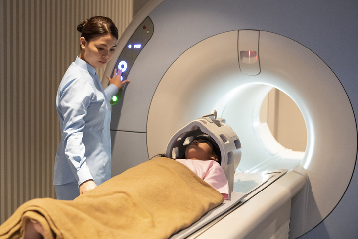 technician operates MRI machine as a girl lays on the examination tray.