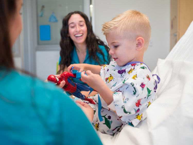 Boy plays with spiderman toy from hospital bed.