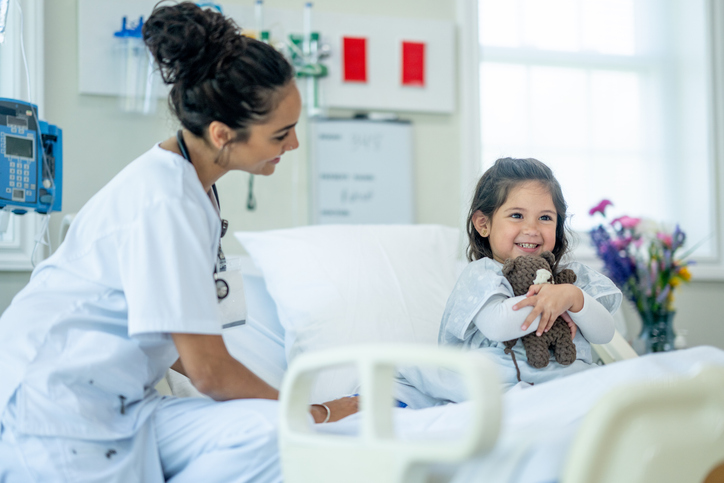 nurse and girl smiling on hospital bed.