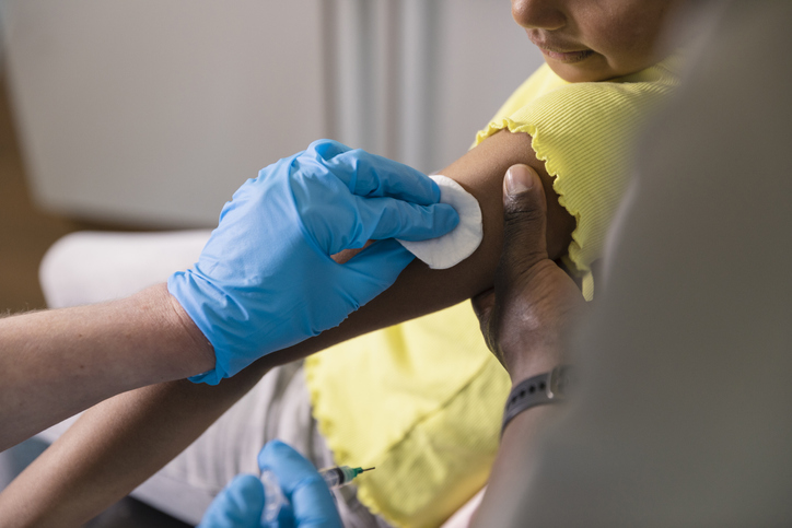 gloved hand wiping a girl's arm with an alcohol pad.