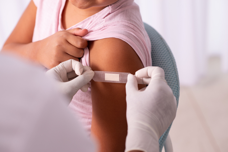 gloved hands placing a band-aid on girl's arm.