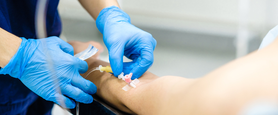 gloved hands of provider about to insert IV into patients arm.