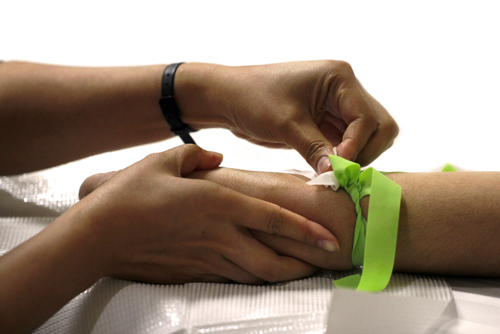 Arm with IV inserted, a cotton patch at insertion point, and the hand squeezing a rubber ball.